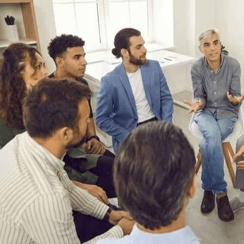 Atelier-de-Sante-Mentale-et-Bien-Etre-en-Entreprise Un groupe de personnes en tenue décontractée et professionnelle assiste à un atelier de bien-être en entreprise, assis en cercle avec un animateur qui parle.